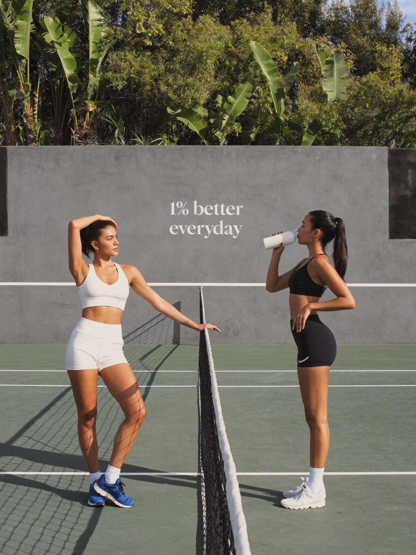 Two women on a tennis court with '1% better everyday' mural — week 3 to 4 of emberly PMOS Support